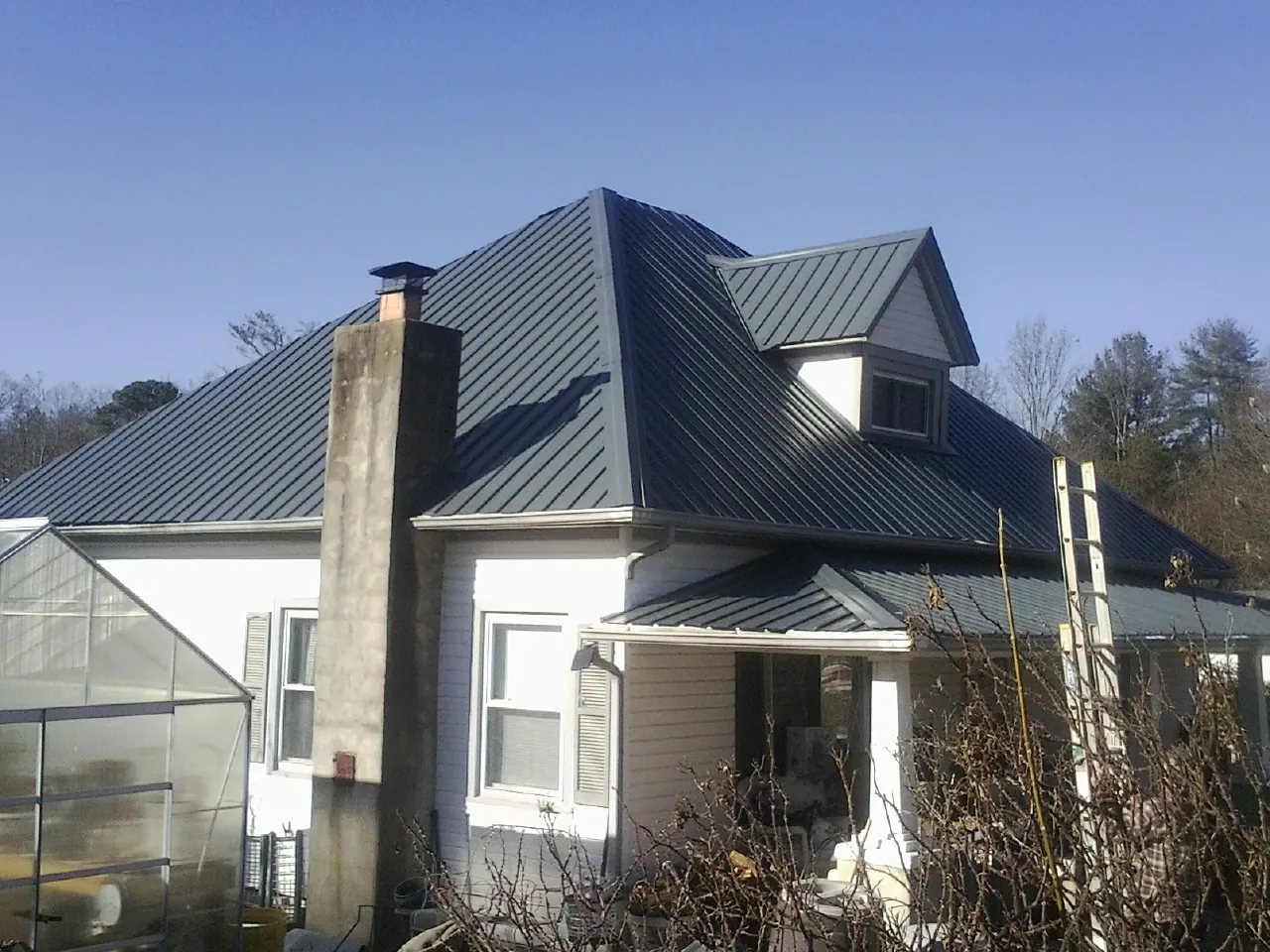 Dark blue standing seam metal roof on a white farmhouse with dormer — Slate & Tile Roof Repair by Roofing Brothers in Palisade